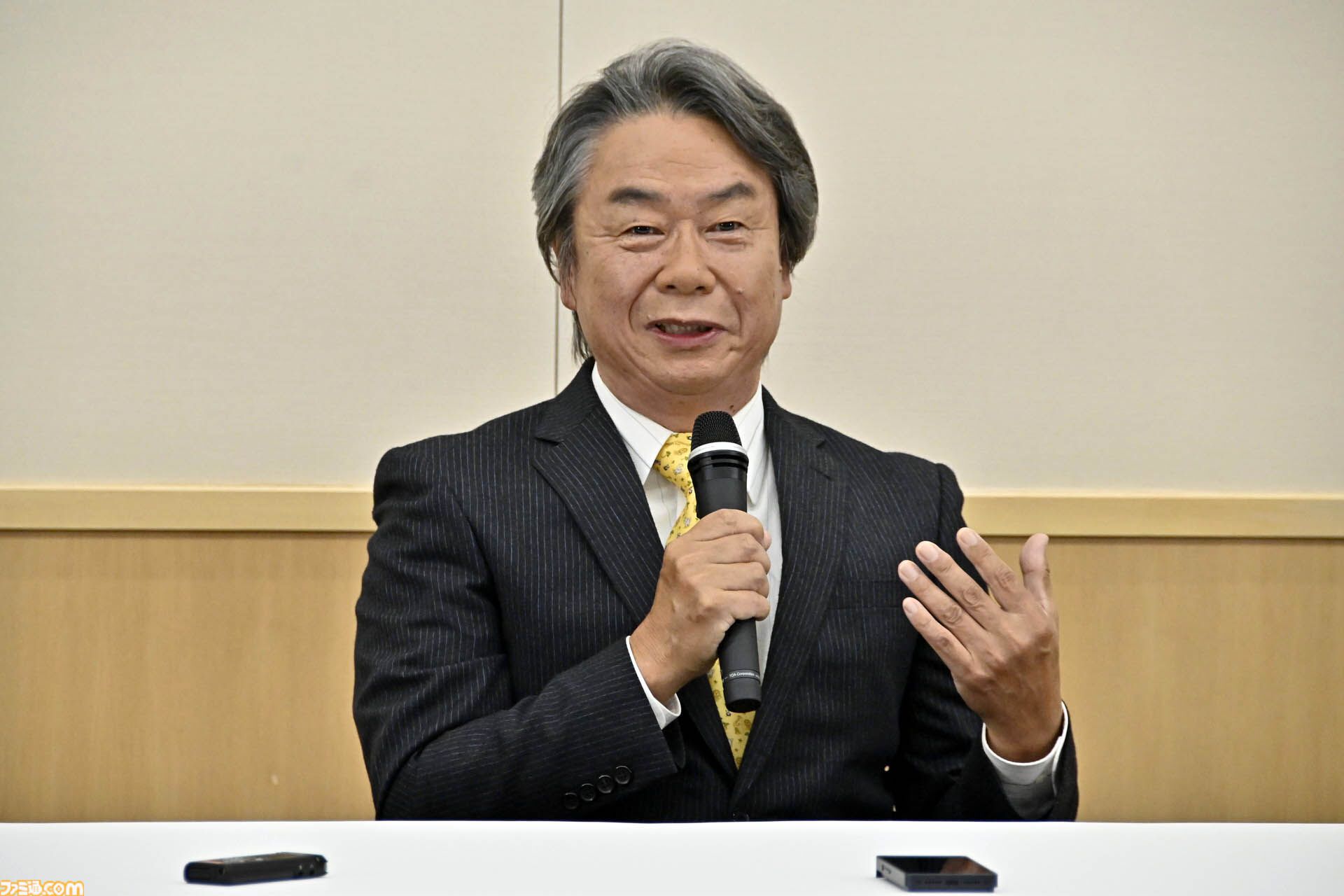 교토 닌텐도 본사 기자회견에서 오른손으로 마이크를 쥐고 왼손을 들어 보이며 질문에 답하는 미야모토 시게루.