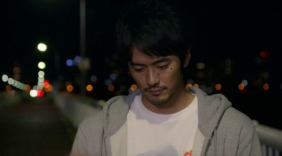 밤 다리 위에서 흰 봉투를 내려다보는 같은 남자. 뒤로 도시의 불빛이 번져 있다.